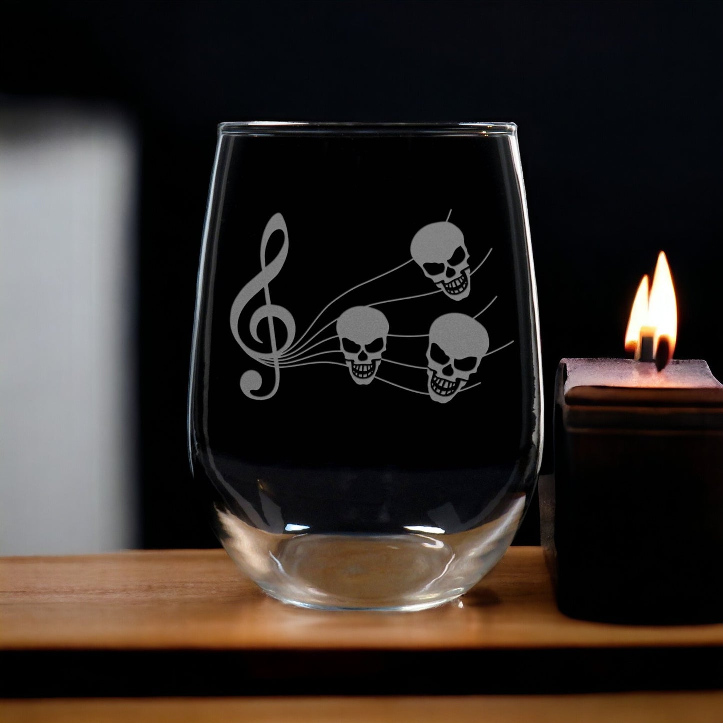 A stemless wine glass with a music staff and skull design, placed on a table near a candle.