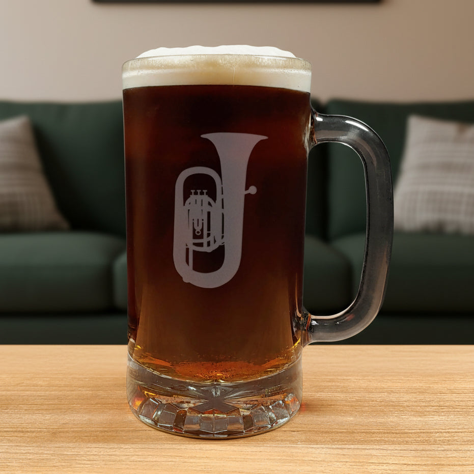 Glass mug with a tuba engraving filled with dark beer on a wooden surface with a green couch in the background