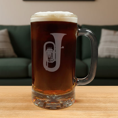 Glass mug with a tuba engraving filled with dark beer on a wooden surface with a green couch in the background