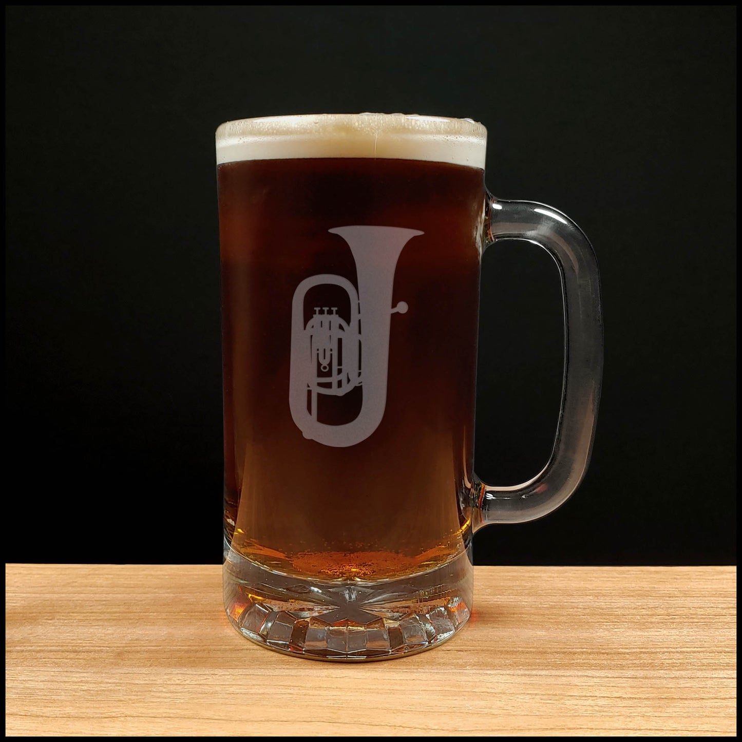 Glass mug with a tuba engraving filled with dark beer on a wooden surface 