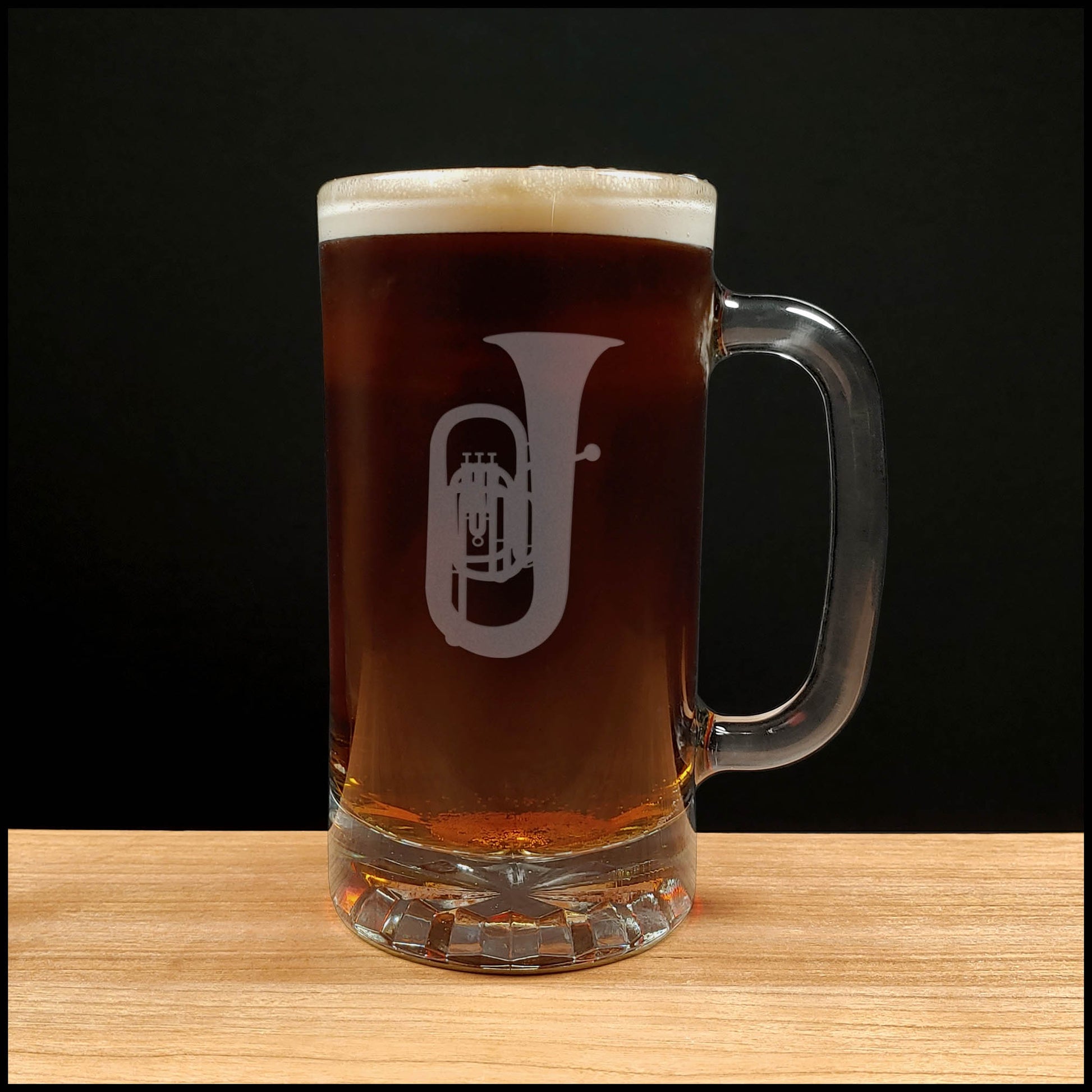 Glass mug with a tuba engraving filled with dark beer on a wooden surface 