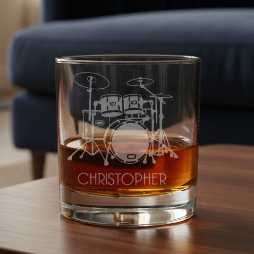 Glass of whiskey with a drum set engraving on a wooden table in a living room.