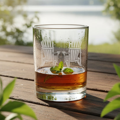 Clear glass with engraved design of two chairs and a table, filled with amber liquid on a wooden surface.