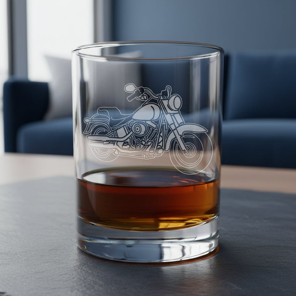 A clear glass rocks tumbler with an etched motorcycle design, partially filled with an amber-colored drink, set on a wooden surface against a dark blue living room.