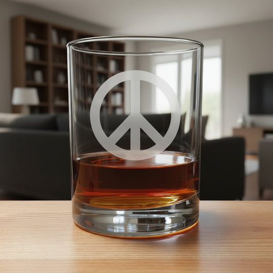 A clear rocks glass with a frosted peace sign, partially filled with amber whiskey, sitting on a light wood surface against a modern living room