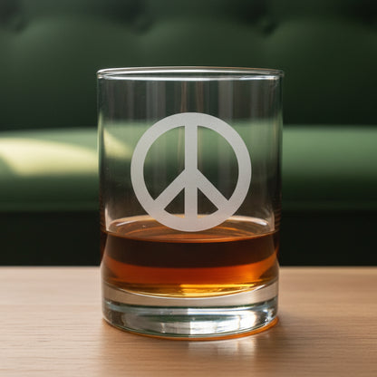 A clear rocks glass with a frosted peace sign, partially filled with amber whiskey, sitting on a light wood surface against a green couch