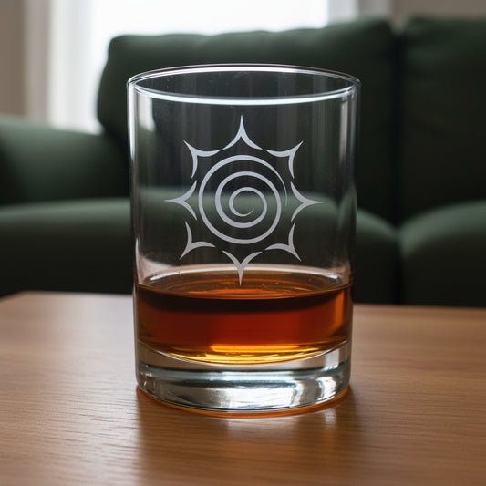 A clear glass rocks tumbler with a white spiral sunburst design, partially filled with amber whiskey, set on a wooden surface against a green couch background.