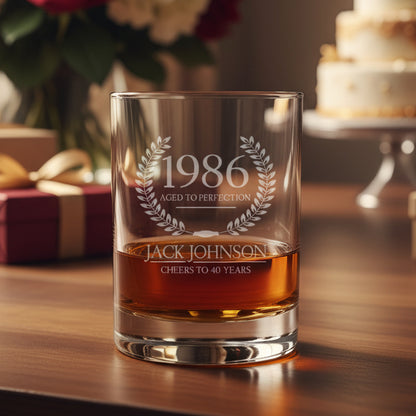 Whiskey glass with engraved text '1986 Aged to Perfection' and 'Jack Johnson Cheers to 40 Years' on a wooden surface.