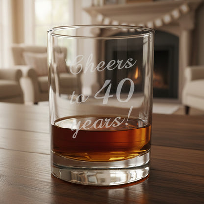 Clear glass tumbler with 'Cheers to 40 years!' engraving, with amber liquid on a wooden surface.