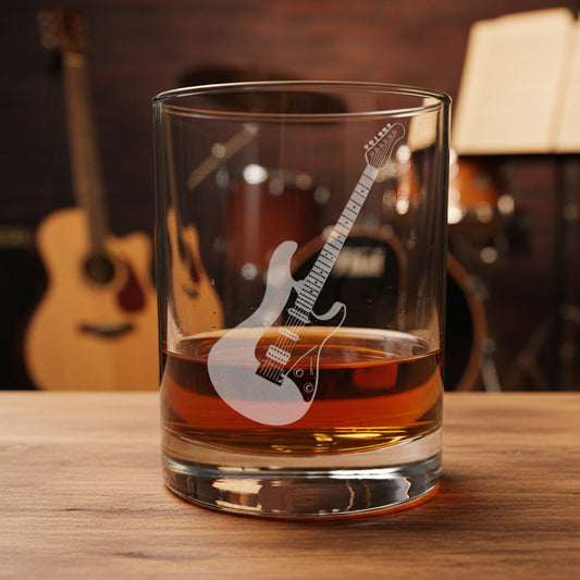 A clear rocks glass with a white electric guitar graphic, filled with amber whiskey and set on a wooden table with a blurred guitar and drum set in the background.