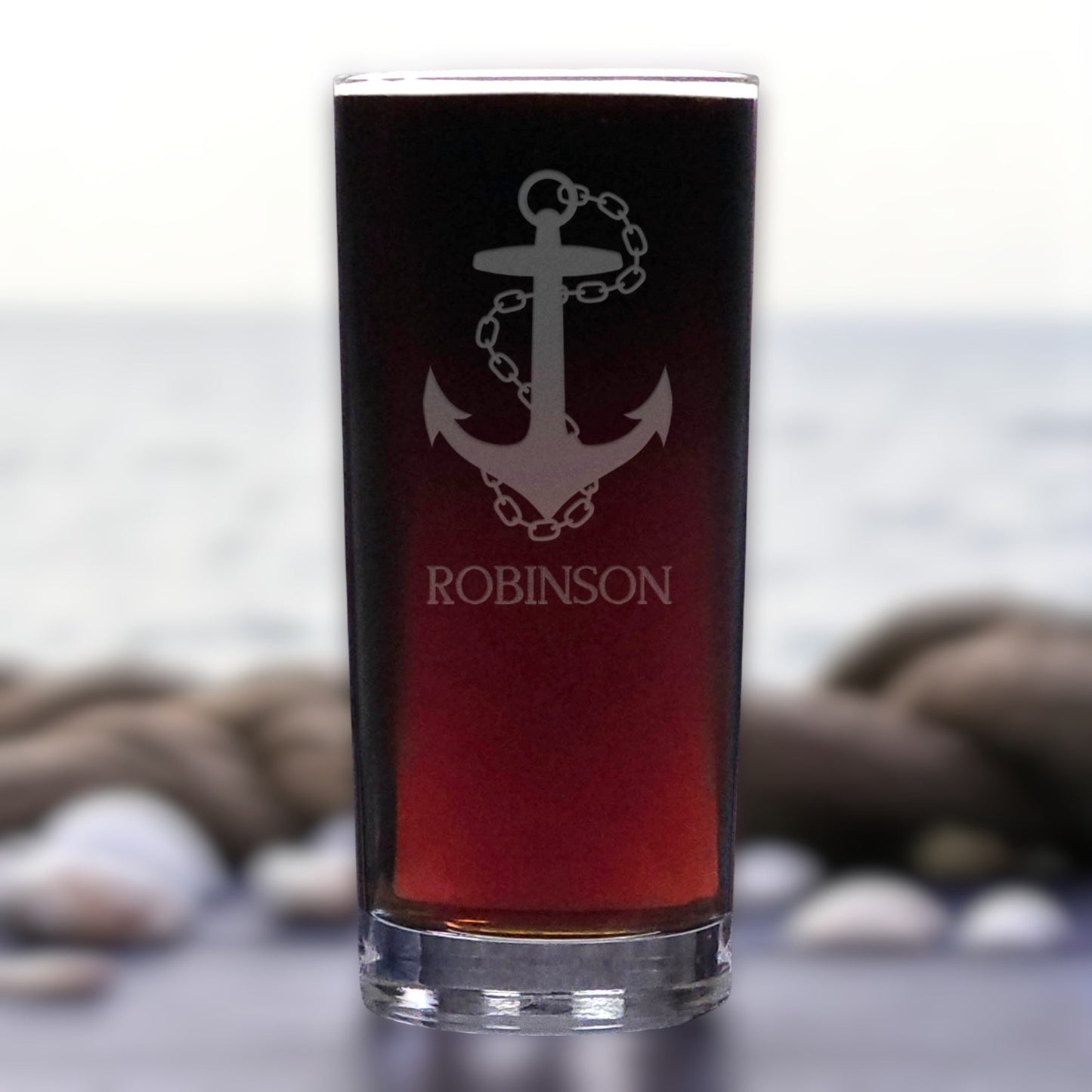 Glass with anchor design and 'ROBINSON' text against a blurred natural background