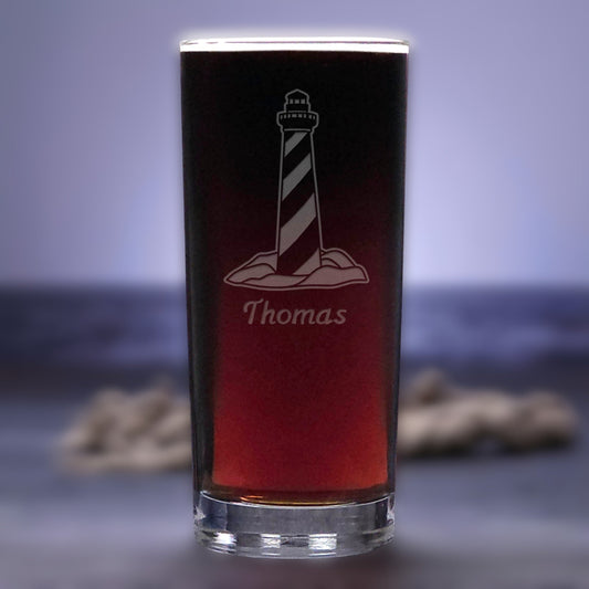 Pint glass with a lighthouse design and 'Thomas' engraving on a blurred background