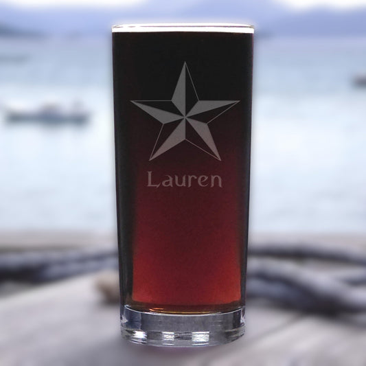 Personalized glass with star design and 'Lauren' engraving, filled with a red liquid, against a blurred natural background.