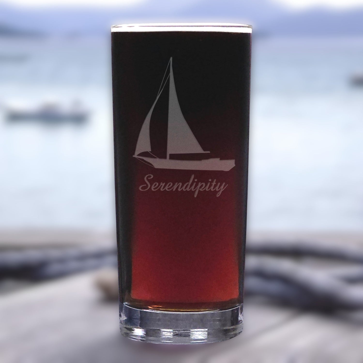 Glass with sailboat design and 'Serendipity' text against a blurred water background