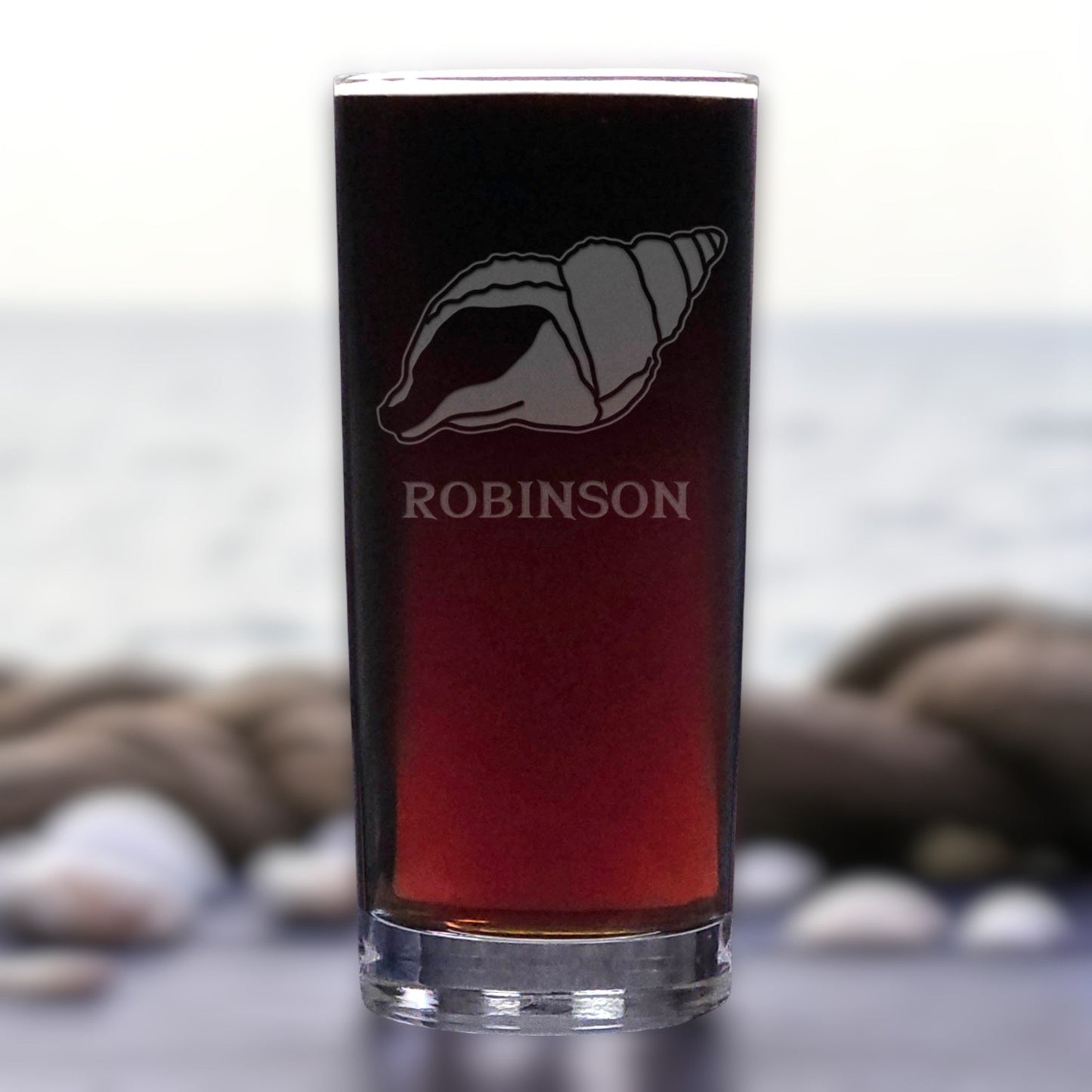 Glass with a shell design and 'ROBINSON' text against a blurred natural background