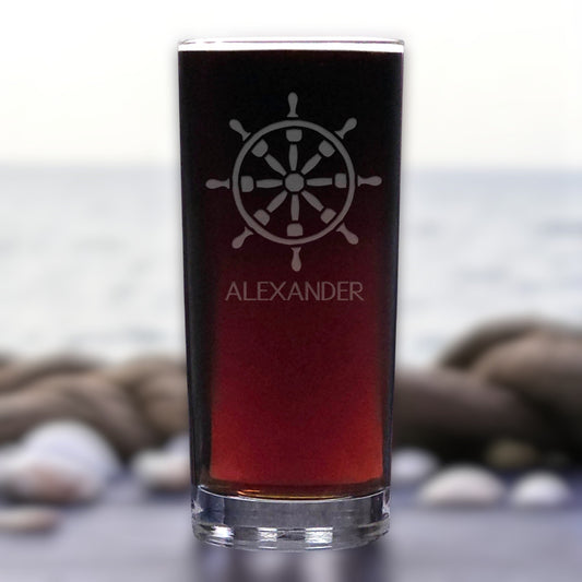 Glass with a ship's wheel design and 'ALEXANDER' text against a blurred natural background