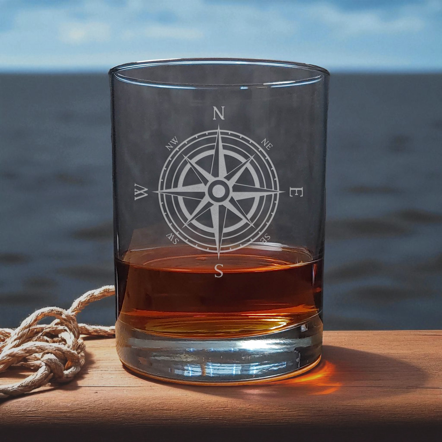 Glass with a compass design filled with amber liquid on a wooden surface with a blurred natural background