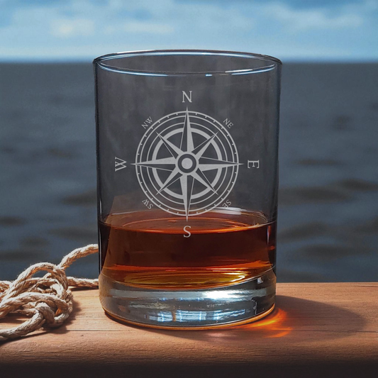 Glass with a compass design filled with amber liquid on a wooden surface with a blurred natural background