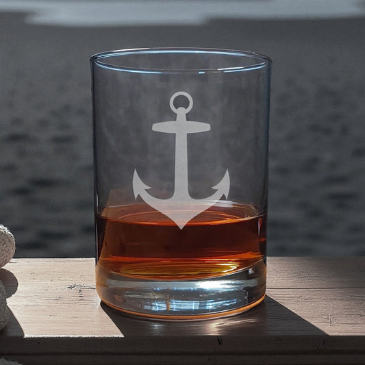 Clear glass with an anchor design filled with amber liquid on a wooden surface.
