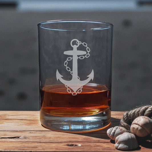Clear glass with anchor design filled with amber liquid on a wooden surface.