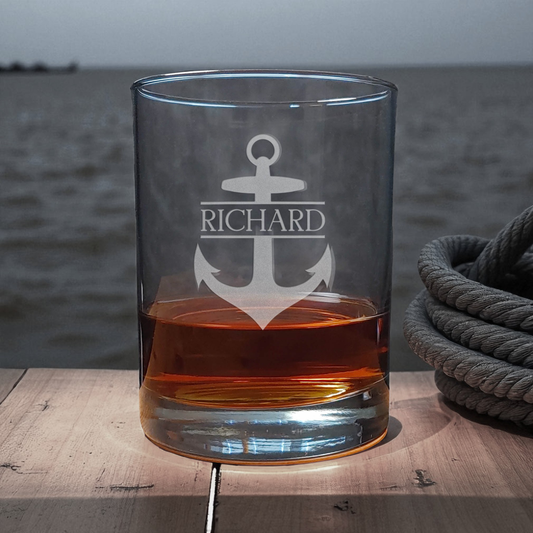 Glass with an anchor design and engraved name 'Richard' on a wooden surface with a water background.