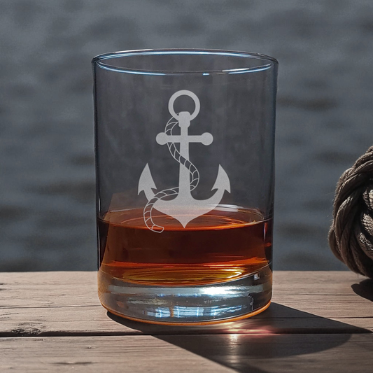 Clear glass with anchor design filled with amber liquid on a wooden surface.