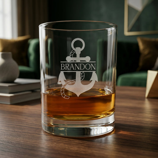 Clear glass tumbler with etched anchor design and 'Brandon' text, filled with amber liquid on a wooden surface.