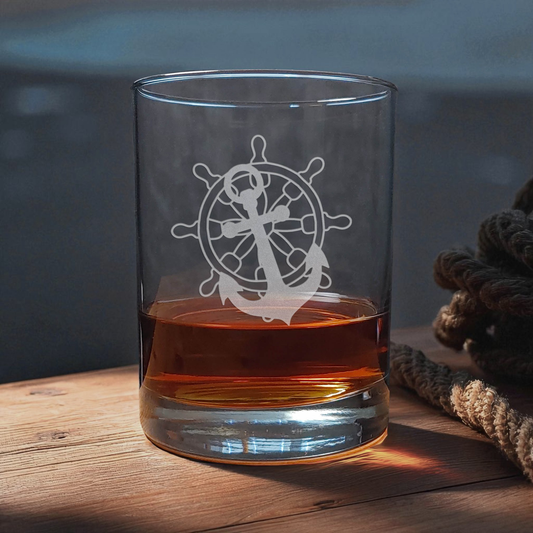 Clear glass with an anchor and wheel design filled with amber liquid on a wooden surface.
