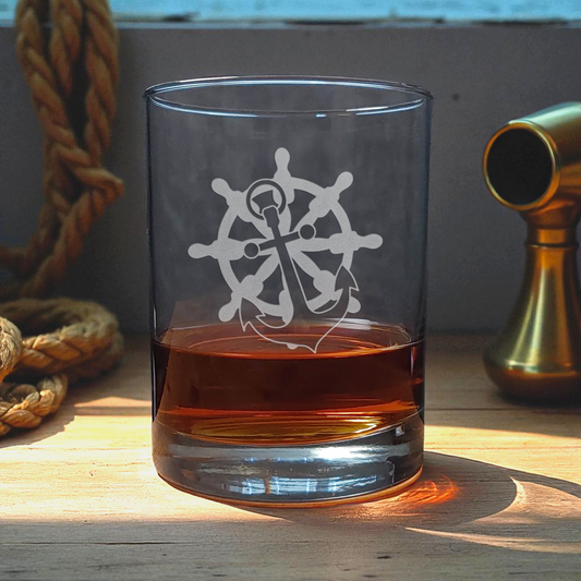 Clear glass with ship's wheel and anchor design filled with amber liquid on a wooden surface.