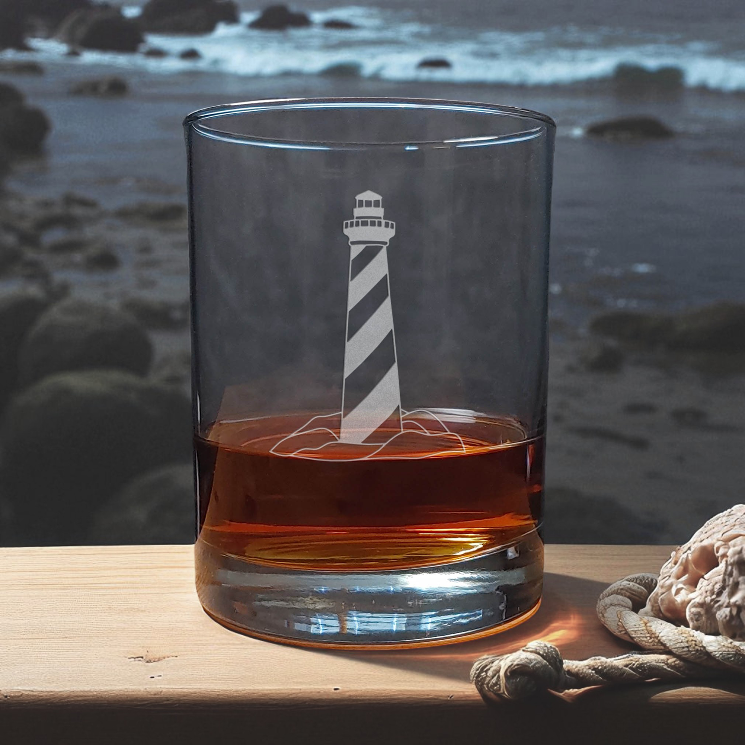 Glass with lighthouse design filled with amber liquid on a wooden surface with a beach background
