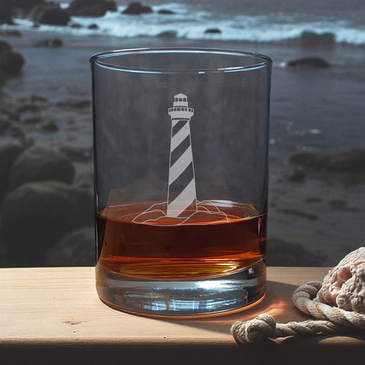 Glass with lighthouse design filled with amber liquid on a wooden surface with a beach background