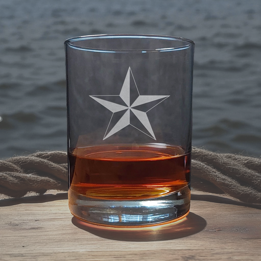 Clear glass with star design filled with amber liquid on a wooden surface with water in the background