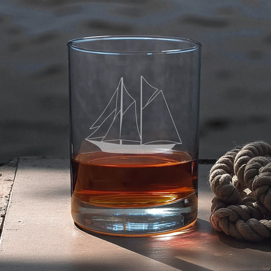 Clear glass with ship etching filled with amber liquid on a wooden surface.