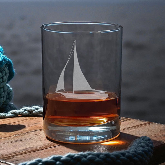 Clear glass with sailboat design filled with amber liquid on a wooden surface.