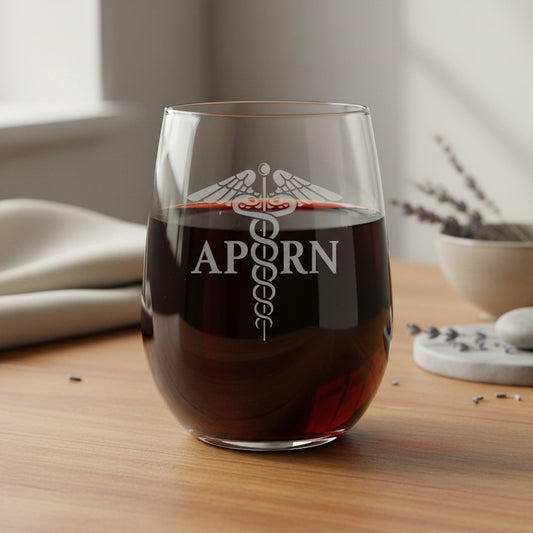 A stemless wine glass filled with red wine sits on a wooden table. The glass is etched with a caduceus symbol and  'APRN'.