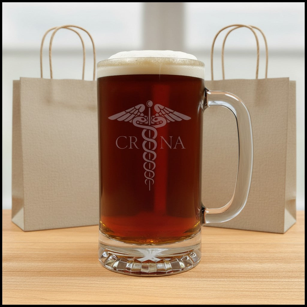 A clear glass beer mug filled with amber beer and topped with white foam, standing on a wooden surface. The mug has a frosted white medical-style emblem and the name 'CRNA' printed on the front.