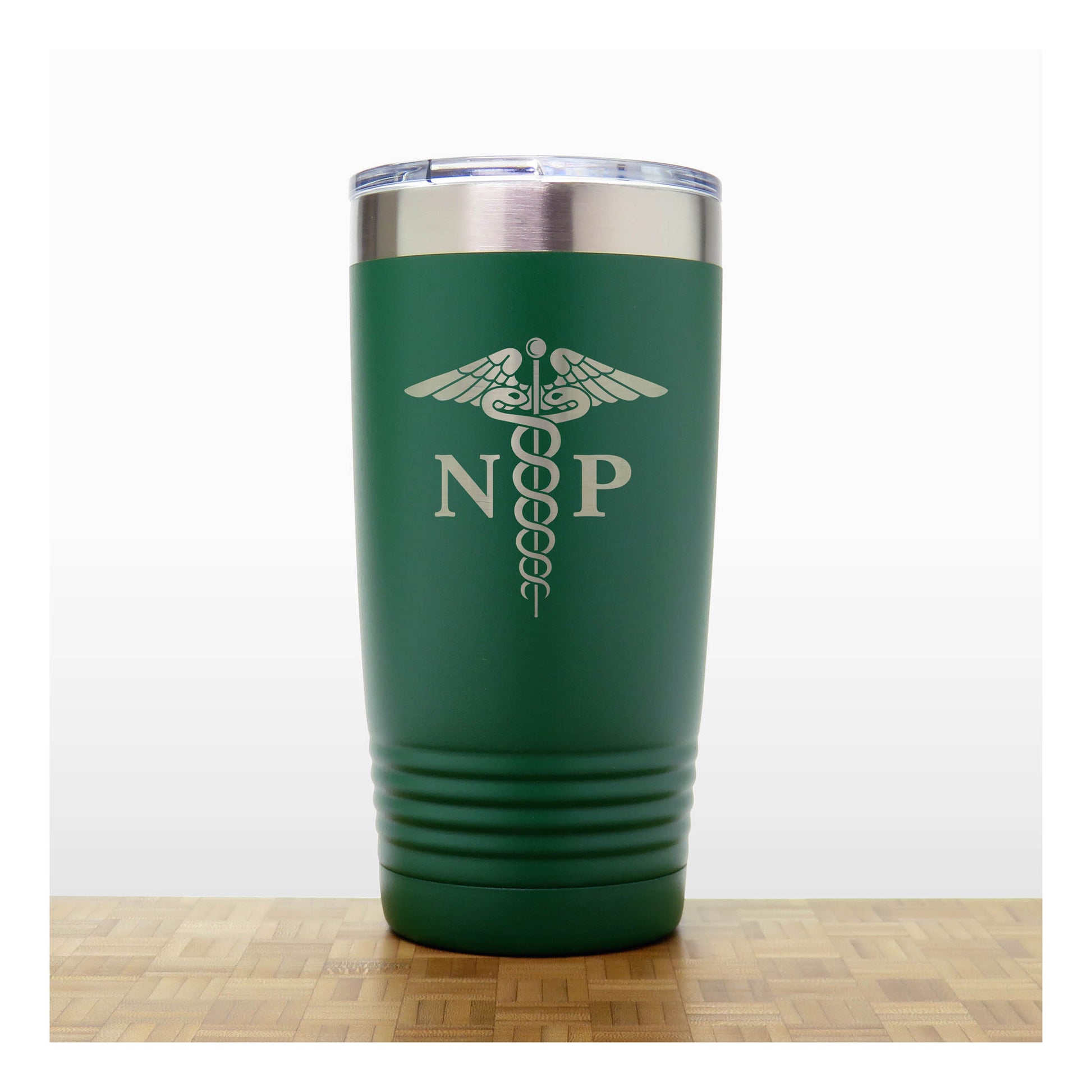A dark green insulated travel tumbler with a stainless steel lid, With an laser engraved  medical caduceus symbol with the letters 'NP' on the front. The tumbler is shown standing on a wooden surface against a white background.
