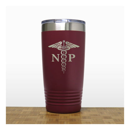 A maroon insulated travel tumbler with a stainless steel rim and a clear lid, with an laser engraved  medical caduceus symbol with the letters 'NP' on the front. The tumbler is shown standing on a wooden surface against a white background.