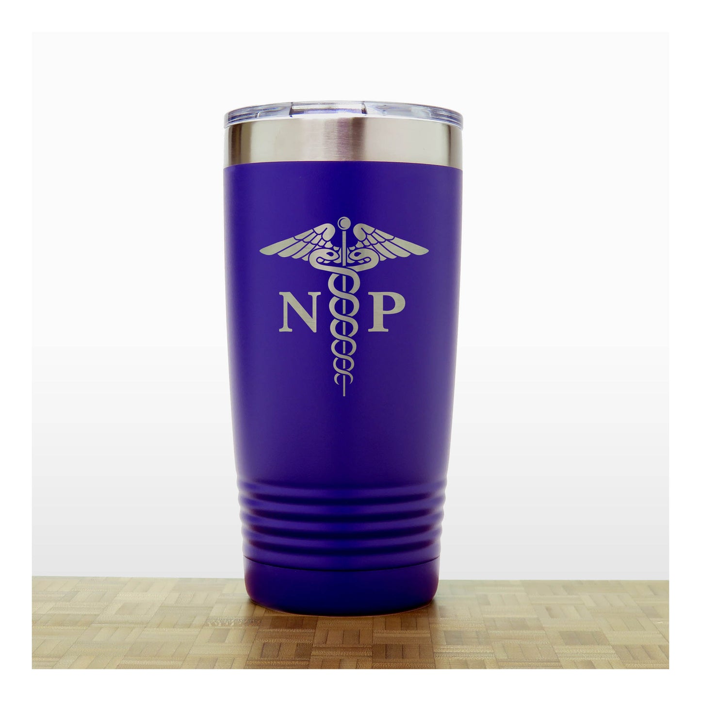 A purple insulated travel tumbler with a stainless steel lid, With an laser engraved  medical caduceus symbol with the letters 'NP' on the front, standing on a wooden surface against a white background.