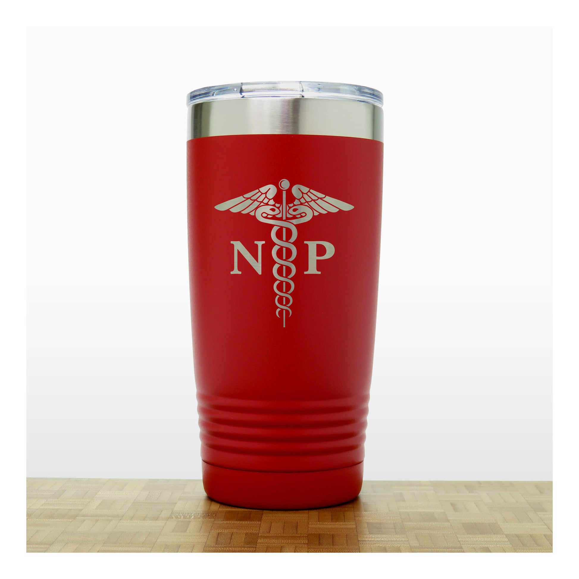 A red insulated travel tumbler with a clear lid, With an laser engraved  medical caduceus symbol with the letters 'NP' on the front, standing on a wooden surface against a white background.