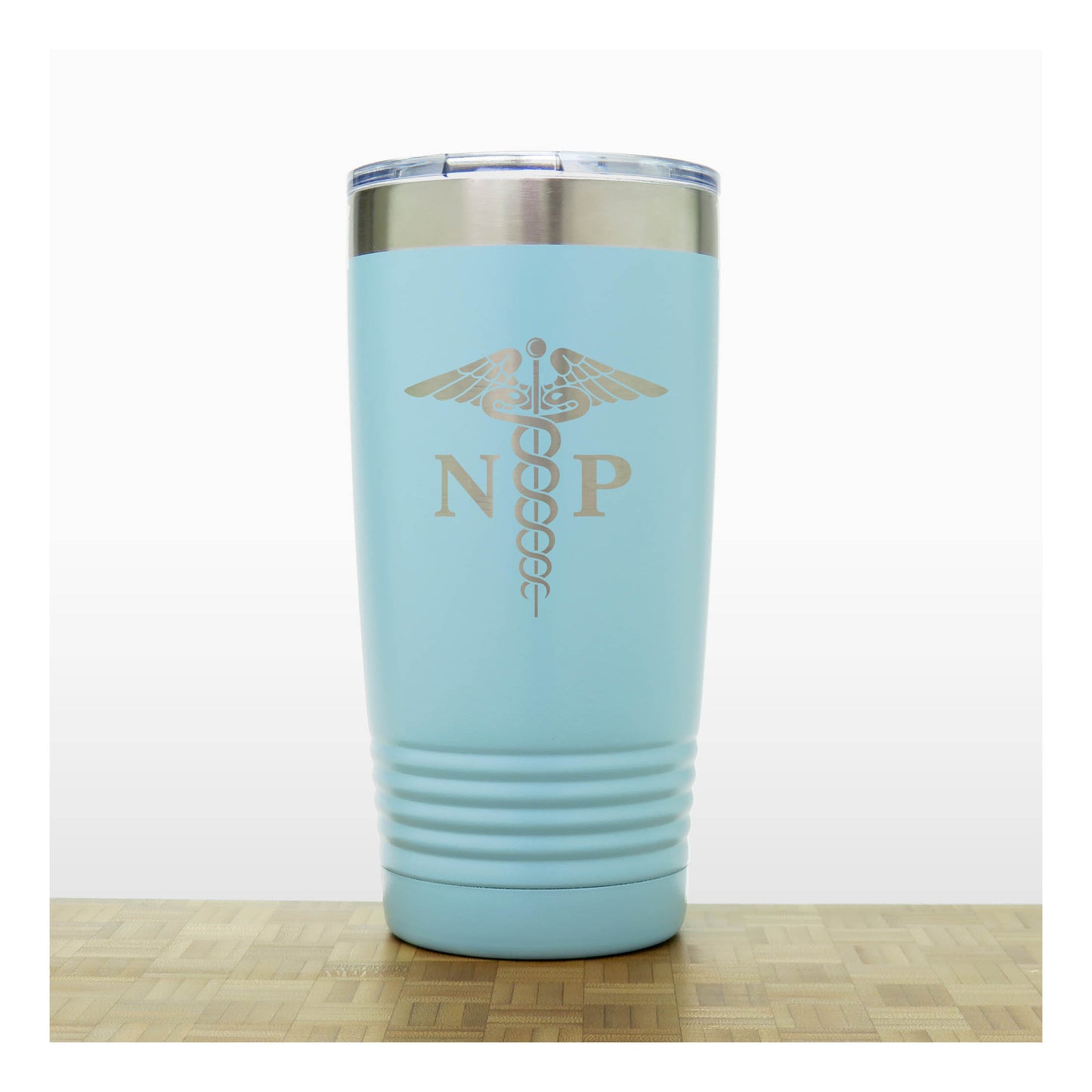 A light blue insulated travel tumbler with a stainless steel rim and a clear lid, With an laser engraved  medical caduceus symbol with the letters 'NP' on the front. The tumbler is shown standing on a light wood surface against a white background.