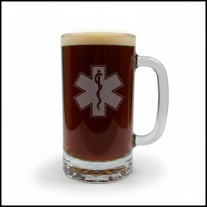 A clear glass beer mug filled with dark brown beer and topped with white foam, featuring a EMS Star of Life with a snake symbol on the front.
