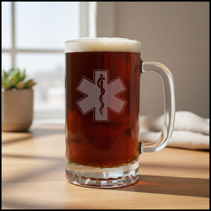 A clear glass beer mug filled with amber beer and topped with white foam, standing on a wooden table. The mug has a EMS Star of Life with a snake wrapped around a rod of Asclepius.