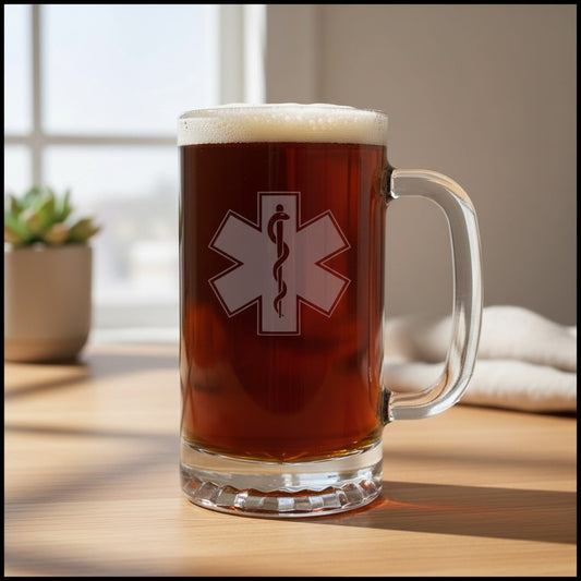 A clear glass beer mug filled with amber beer and topped with white foam, standing on a wooden table. The mug has a EMS Star of Life with a snake wrapped around a rod of Asclepius.