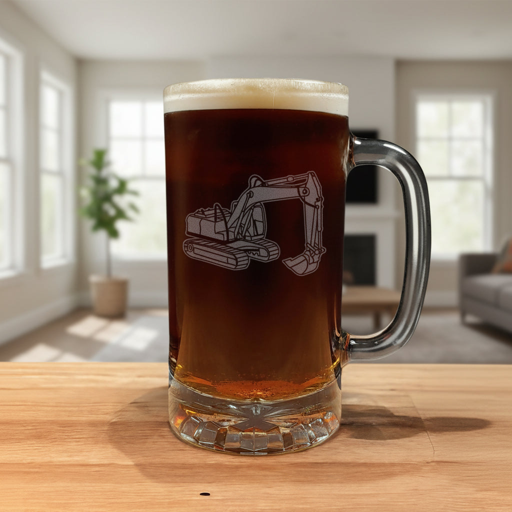 A clear glass beer stein mug with a handle, filled with dark brown beer and topped with white foam, featuring an etched excavator design. The mug sits on a wooden surface against a modern living room
