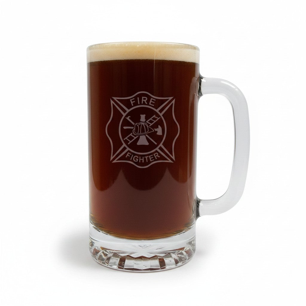 A clear glass beer mug filled with dark brown beer, featuring a an etched Maltese cross firefighter emblem on the front. The mug has a thick handle and is set against a plain white background.