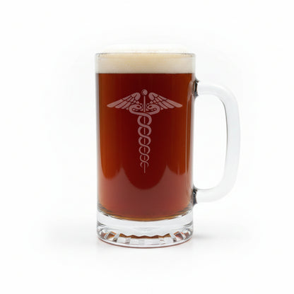 A clear glass beer mug filled with dark amber beer and topped with white foam, featuring an etched medical caduceus symbol on the front, set on a light wood surface against a white background.