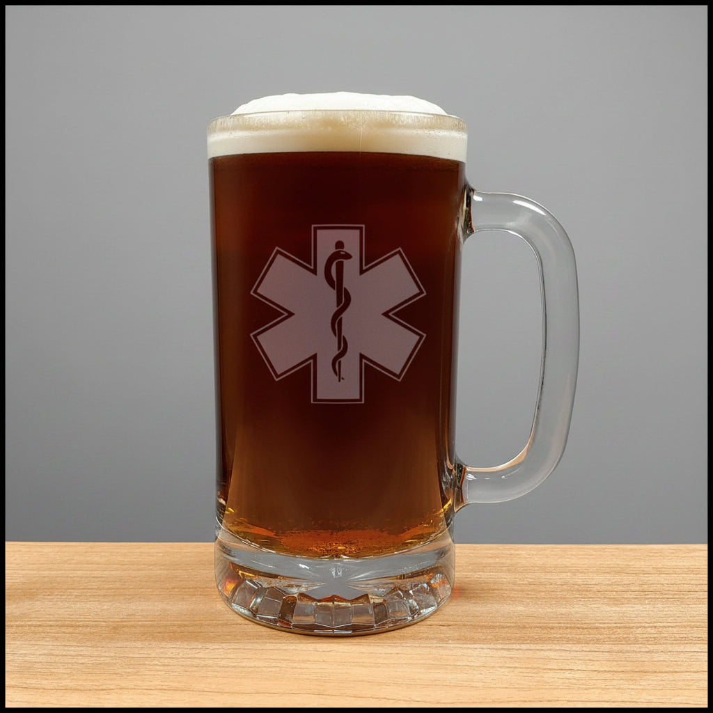 A clear glass beer mug filled with dark amber beer and topped with white foam, featuring a white Star of Life with a black snake design on the front. The mug sits on a light wood surface against a solid grey background.