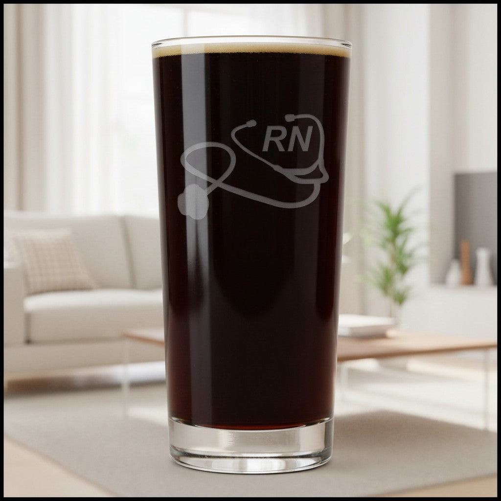 A clear highball glass filled with dark brown coffee, featuring a frosted white graphic of a stethoscope and the letters 'RN' on the front. The glass is set against a softly blurred living room background.
