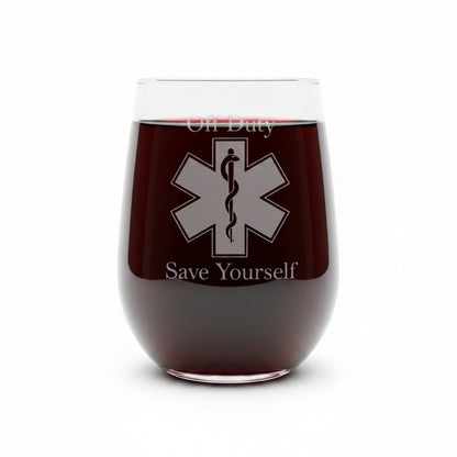 A clear stemless wine glass with a etched EMS symbol with "Off Duty" above the symbolb and "Save Yourself" below. Shown on a white surface against a white background 